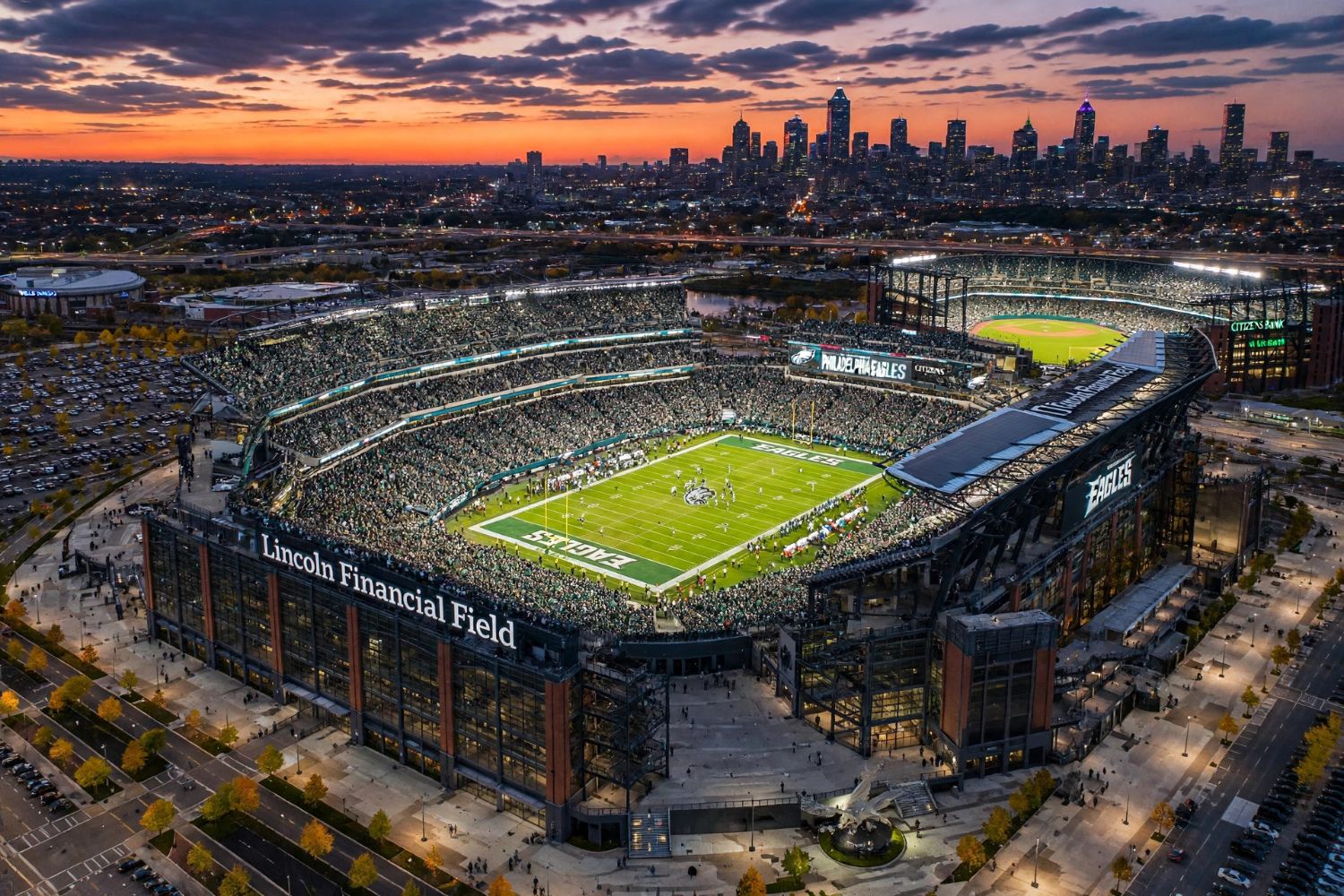 Lincoln Financial Field lit up and packed at dusk, the Philadelphia skyline glowing behind it